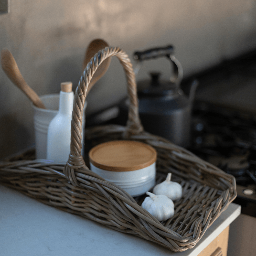Wicker basket with kitchen items including a white container and garlic on a countertop.